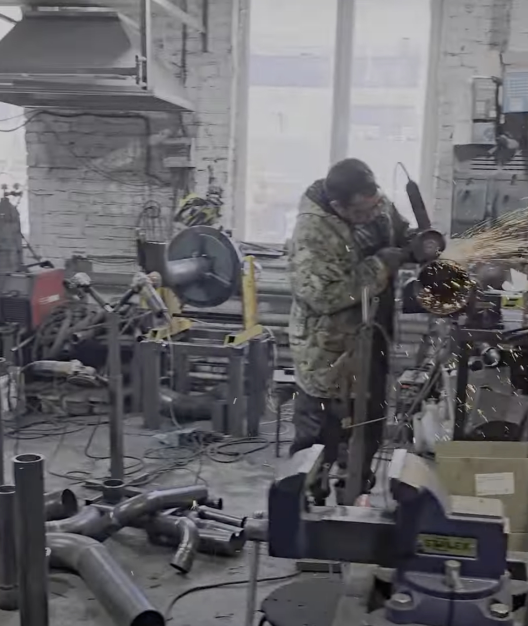 Мужчина в камуфляжной куртке выполняет металлообрабатывающие работы в производственном помещении