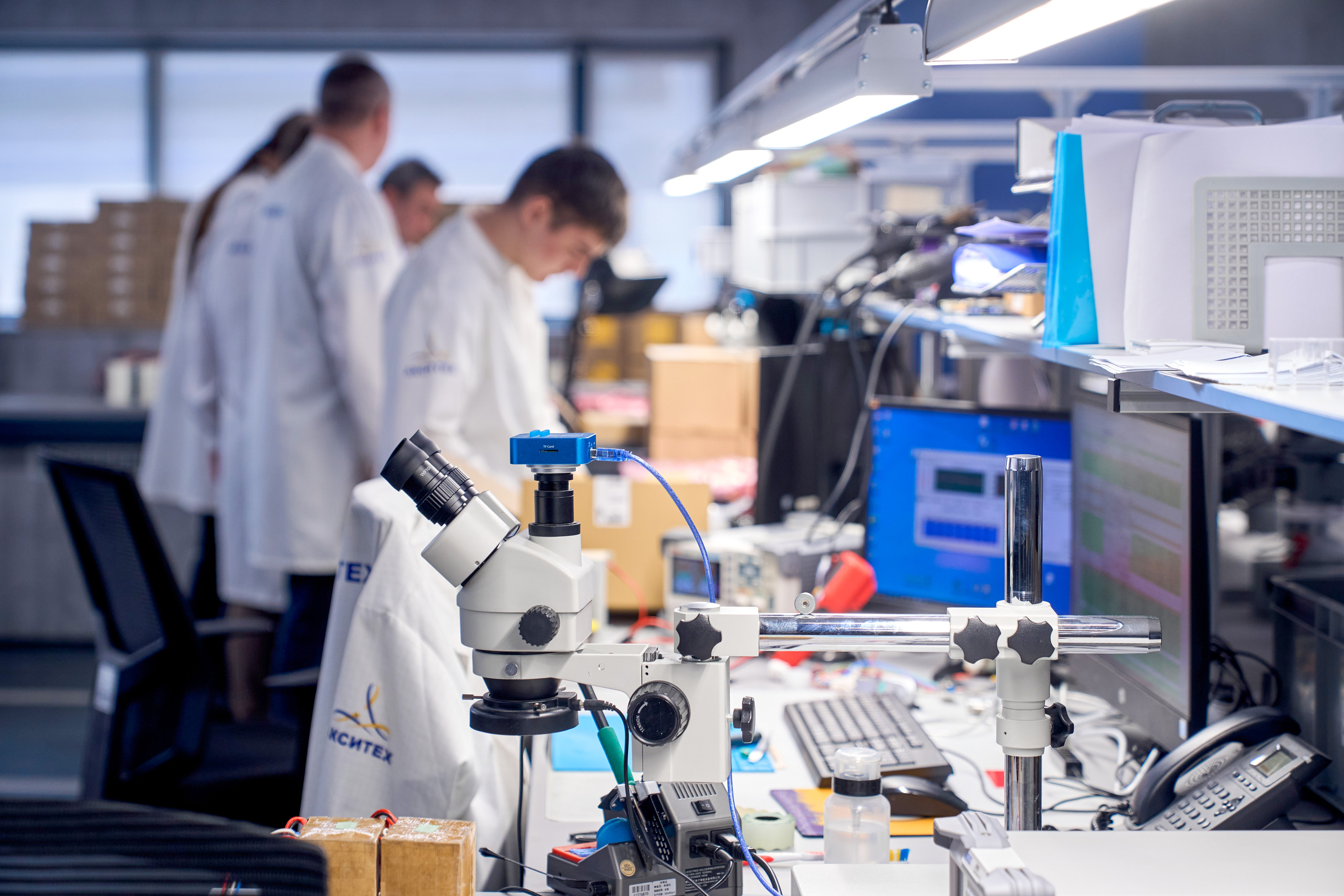 Рабочее место в технопарке в лаборатории электроники с микроскопом, компьютерами и инструментами, где инженеры занимаются тестированием и сборкой устройств