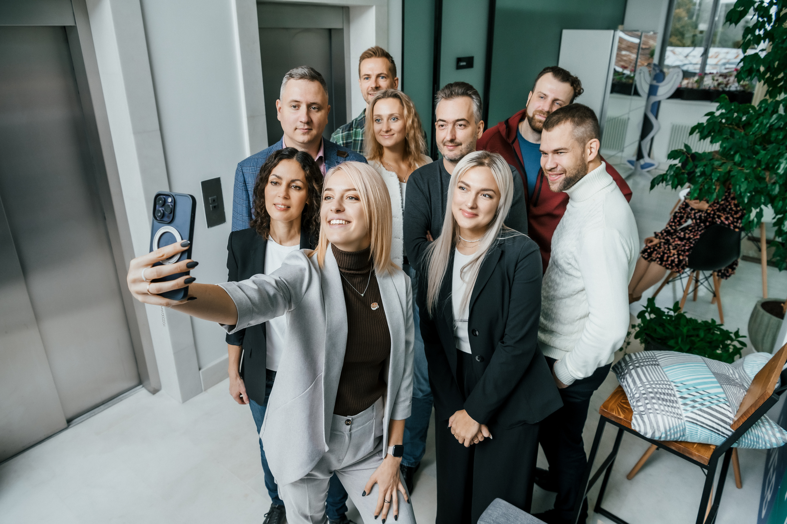 Сотрудники компании фотографируются вместе в офисе на мобильный телефон