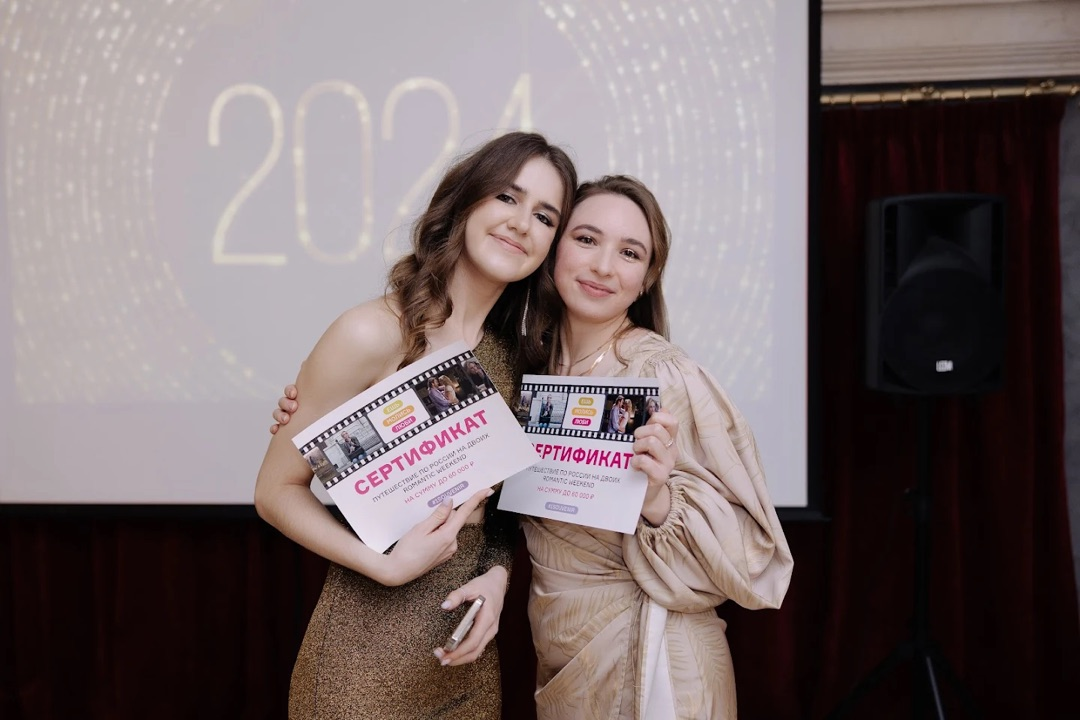 Две девушки, победительницы конкурса «Ешь. Молись. Люби», держат подарочные сертификаты