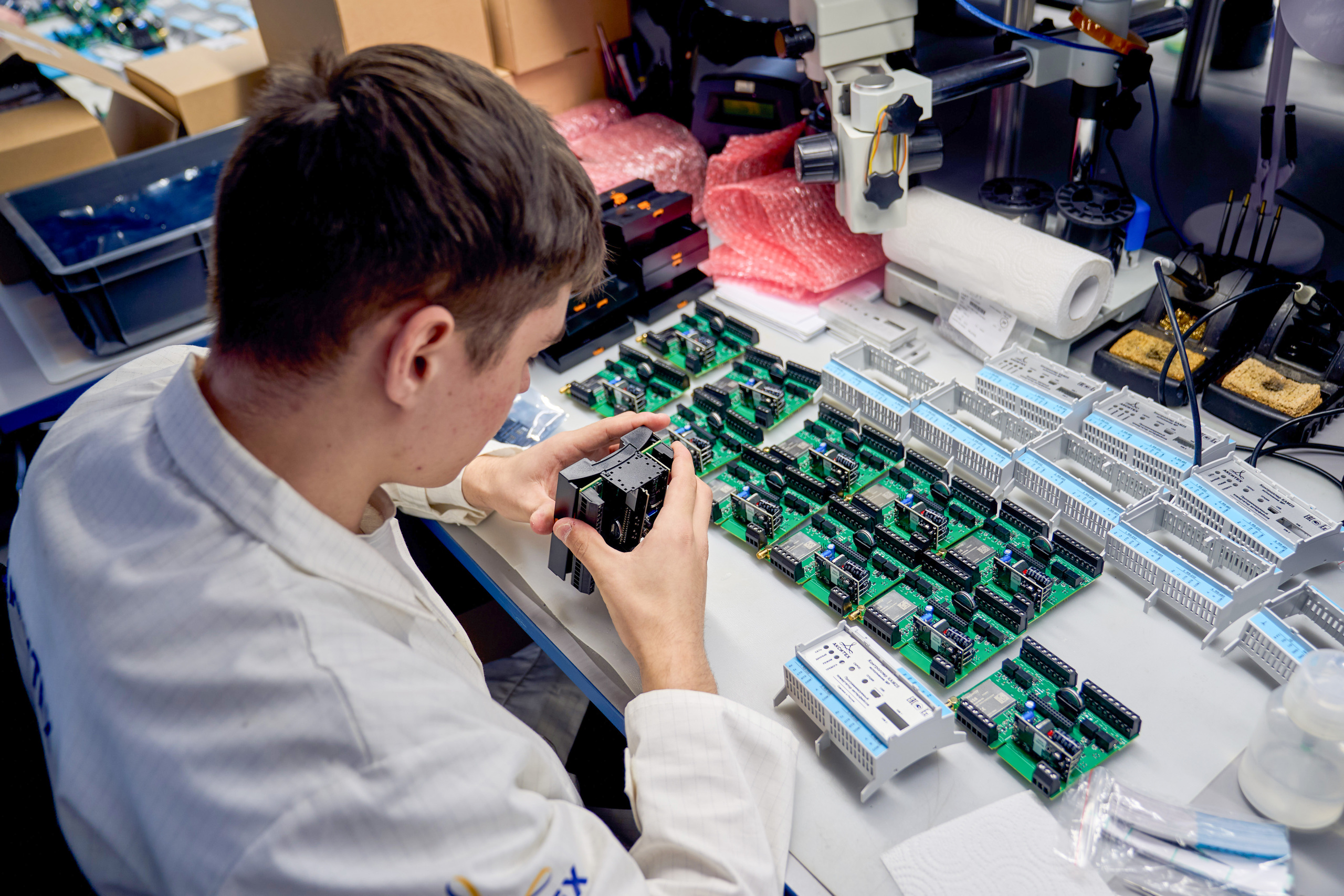 Инженер на рабочем месте собирает и тестирует электронные устройства, используя печатные платы и специализированные инструменты