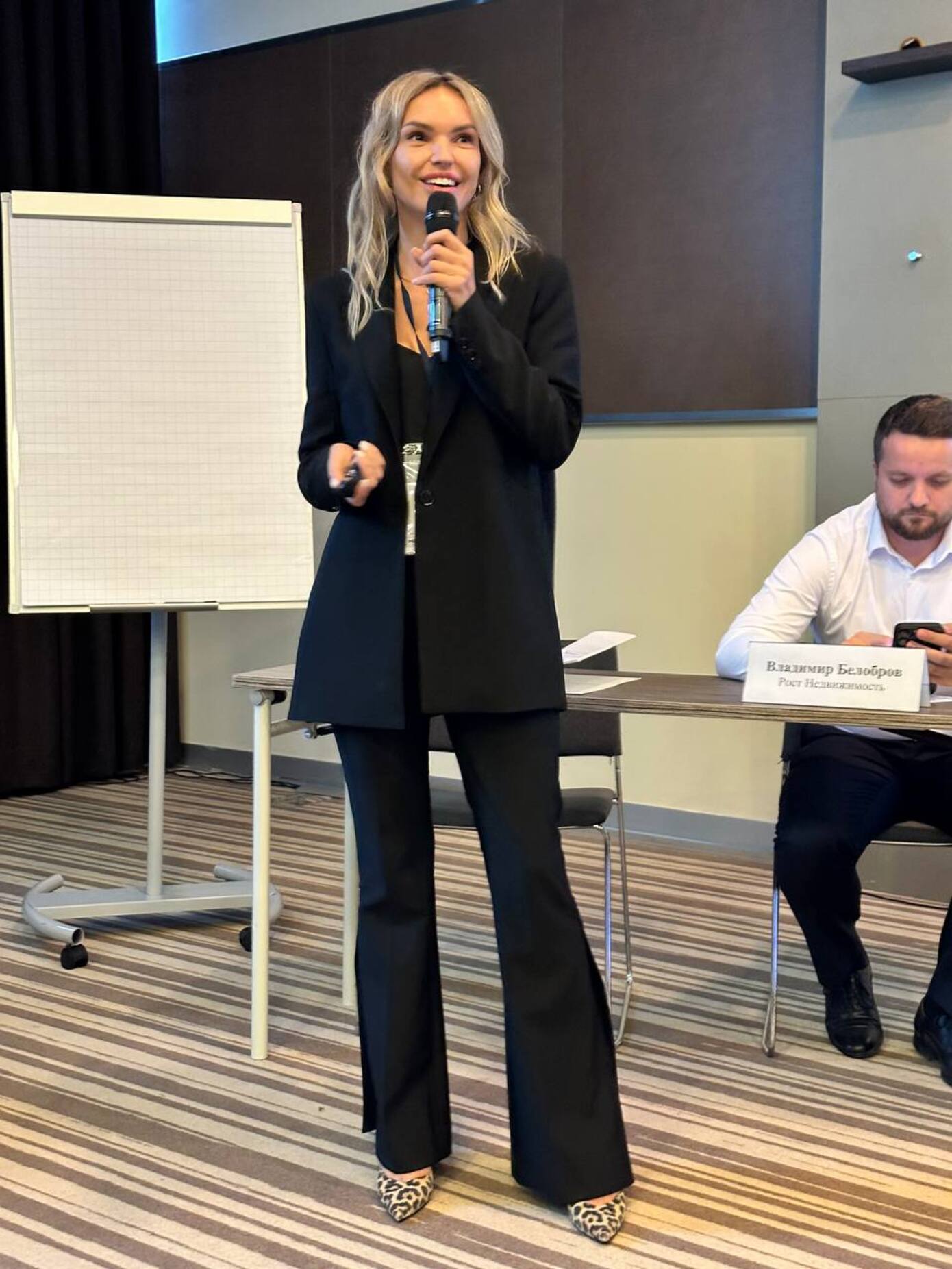 Женщина в костюме, держит в руке микрофон