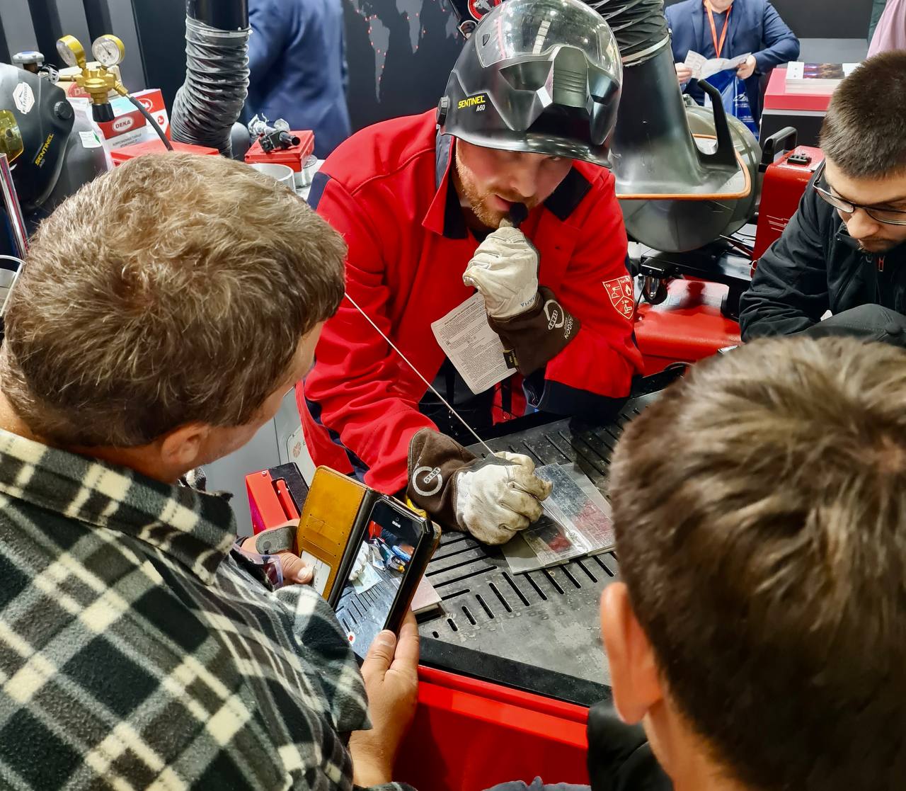 На фото специалист в защитной экипировке объясняет студентам работу на сварочном оборудовании и технологии