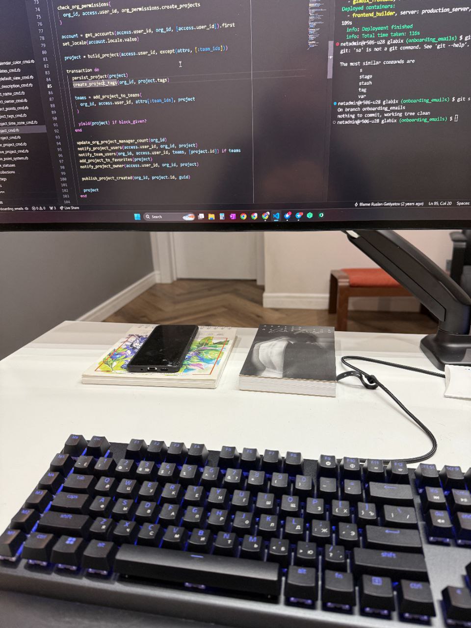 Компьютерный монитор с кодом и рабочий стол с клавиатурой, книгами и ноутбуком