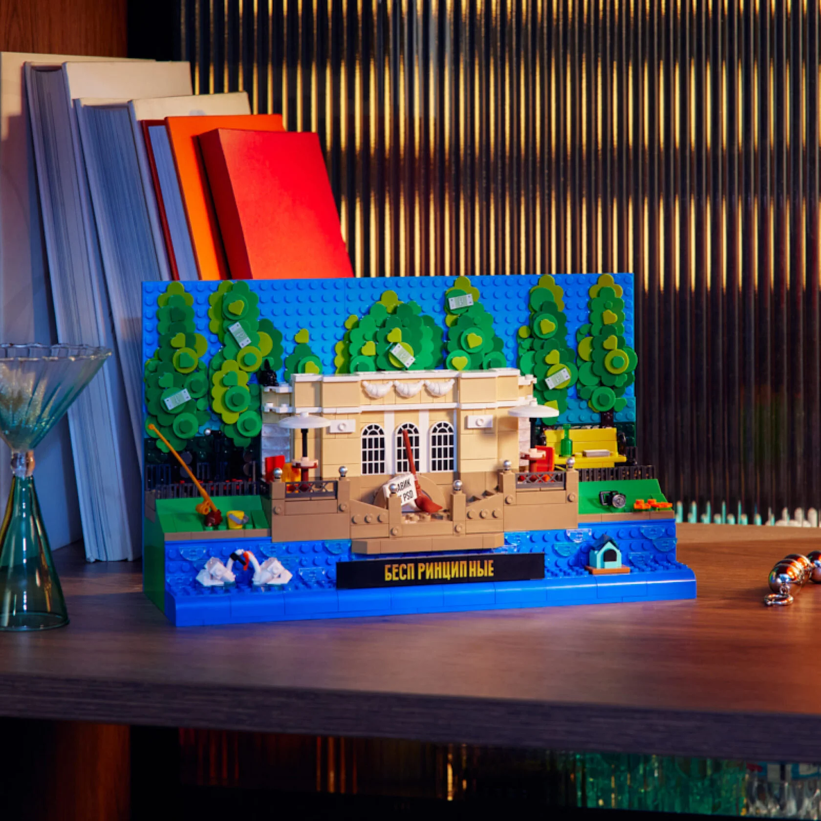 Собранный из конструктора «РУБРИК» набор «Беспринципные», изображающий сцену на Патриарших прудах, стоит на деревянной полке