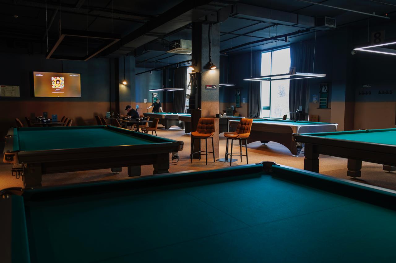 Интерьер бильярдного клуба с несколькими столами, барными стульями и мягким освещением
