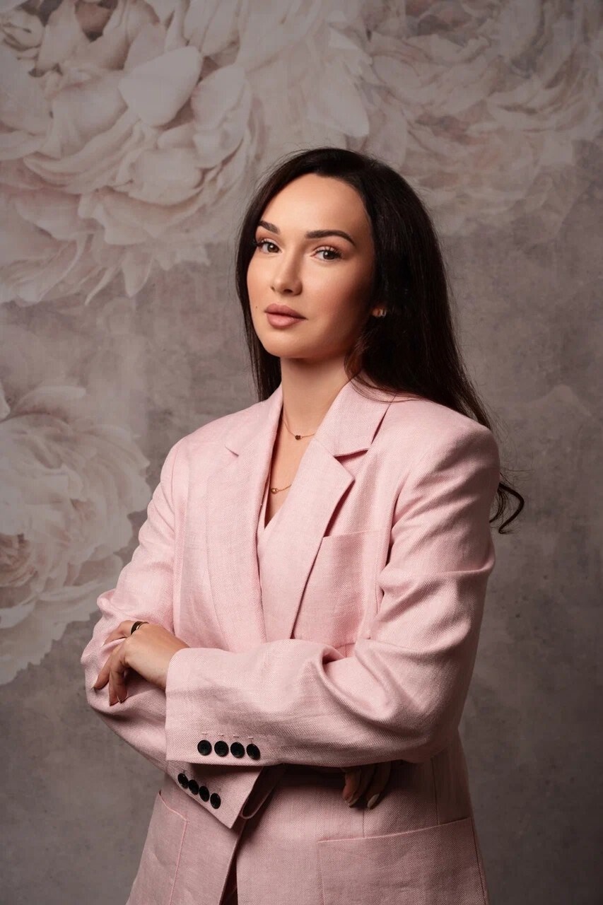 Девушка в розовом пиджаке на фоне стены с цветами