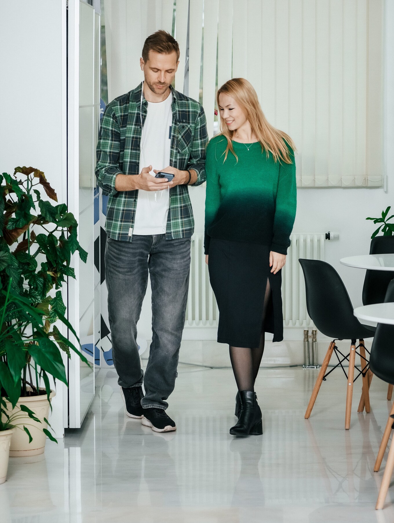 Парень и девушка идут в офисе и смотрят информацию в телефоне