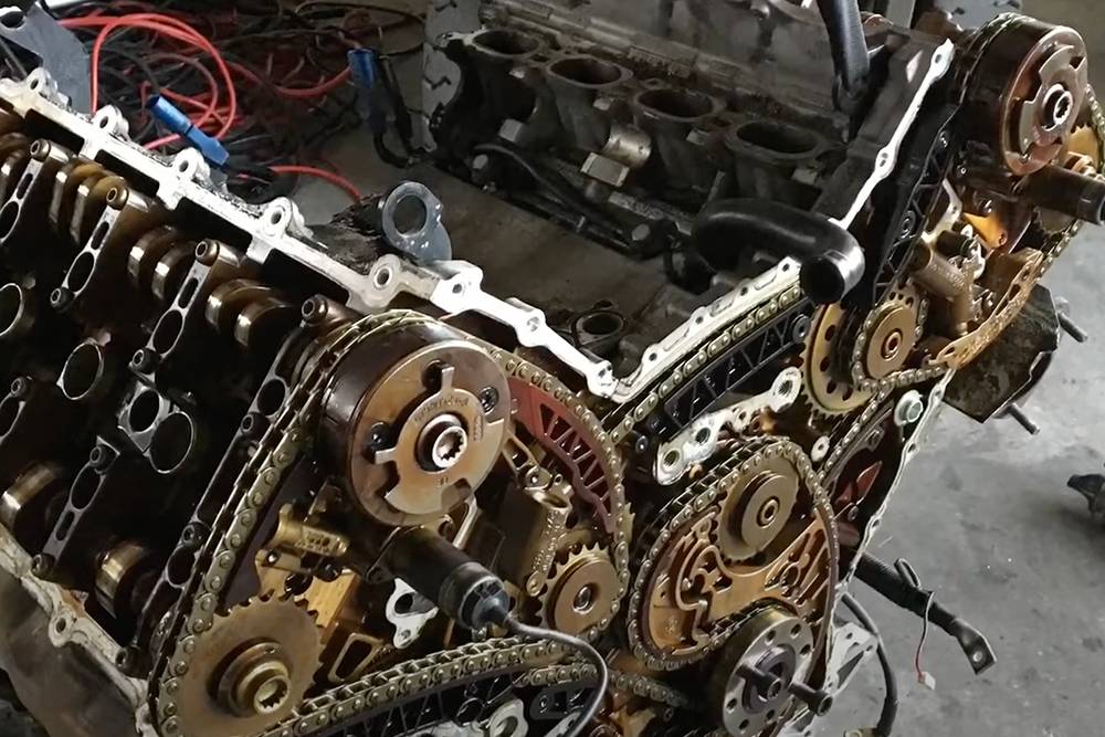 Двигатель Ауди S4 V8 4.2 с четырьмя распредвалами: по два на впускные и выпускные клапаны. Приводная цепь — справа снизу на фото — передает вращение от коленвала к распредвалам через шестерни. Распредвалы приводят в движение отдельные цепи — по одной на два распредвала, на фото — справа и слева. Внизу в центре короткая цепь насоса охлаждения. Источник: ютуб-канал Ивана Визера