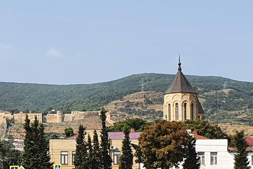 Башня со шпилем — бывшая христианская церковь. Внутри — музей ковров. На заднем плане видна крепость Нарын-Кала
