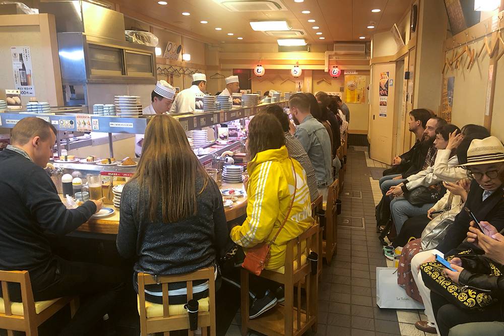 В очереди даже можно сидеть. Справа на фото — очередь на посадку в суши-баре Sushi no Musashi в Киото