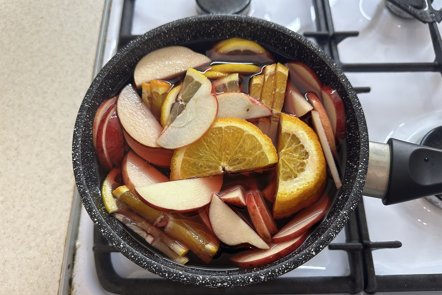 Шаг 1. Лимон, апельсин и яблоко нарежьте дольками. В кастрюлю вылейте сок, добавьте фрукты. Поставьте на плиту, на среднем огне доведите почти до кипения