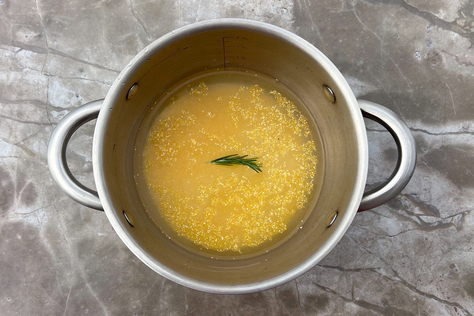 Шаг 1. Крупу всыпьте в кастрюлю, сотейник или глубокую сковороду, положите веточку розмарина. Залейте 500 мл воды или бульона и поставьте на средний огонь