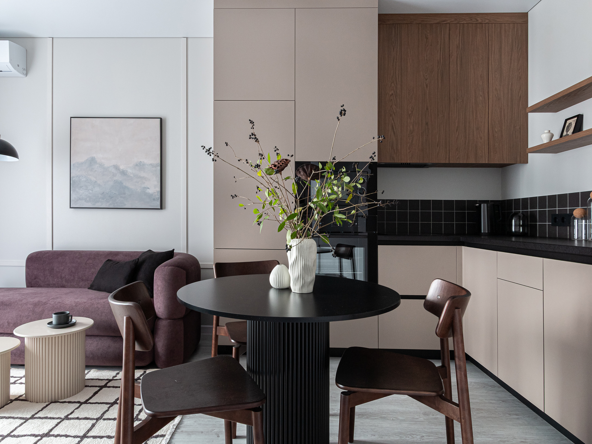 В этом интерьере достаточно прямых линий: это и молдинги на стене, и принт на ковре, и чистые формы кухни. Все линии повторяются: клетка на ковре похожа на ту, что на плитке фартука, только инвертирована по цветам. При этом на ковре она менее строгая