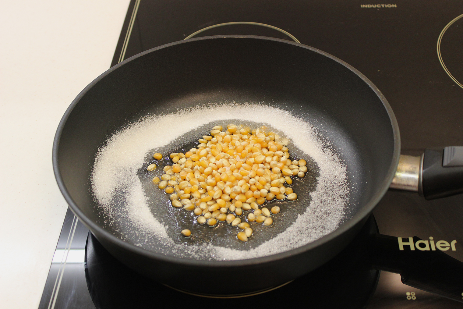 Шаг 1. Масло разогрейте в сковороде на огне выше среднего. Кукурузу, сахар и соль добавьте и накройте крышкой: это нужно, чтобы сохранить жар в посуде и не обжечься, когда зерна начнут взрываться