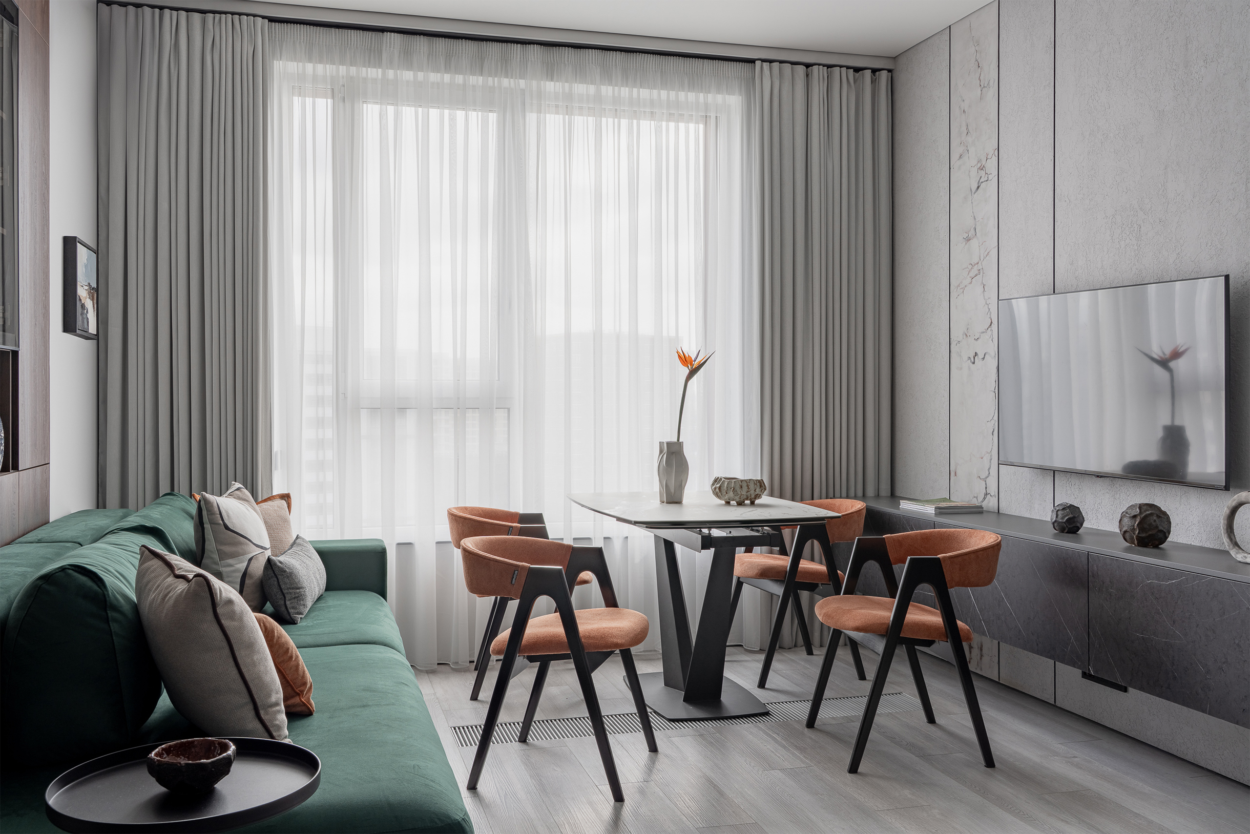 Зеленый диван и оранжевые стулья — акцент, который на сером фоне выглядит еще ярче