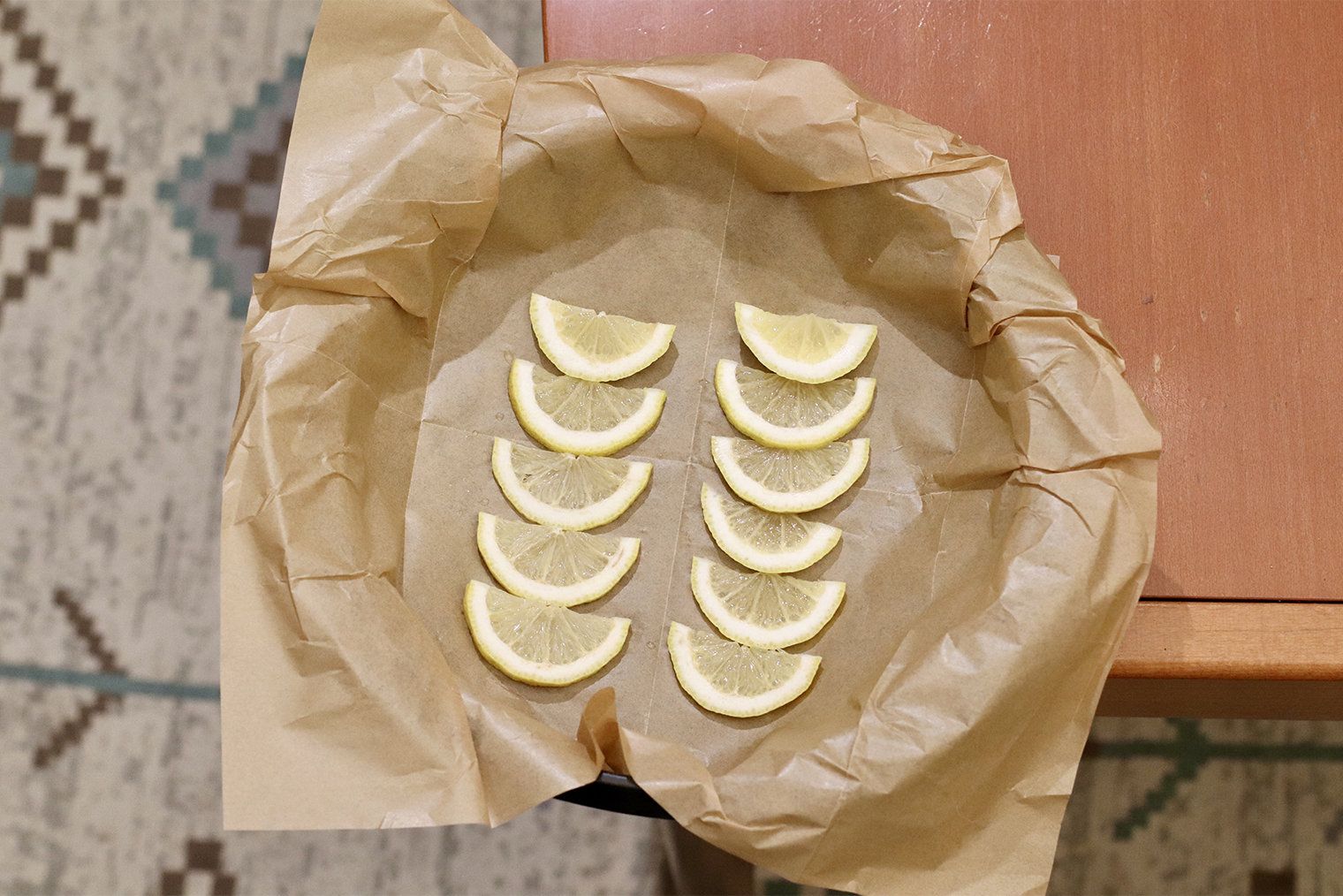 Шаг 2. Форму застелите бумагой для выпечки так, чтобы содержимое можно было завернуть в бумагу. Лимон нарежьте ломтиками и выложите в форму