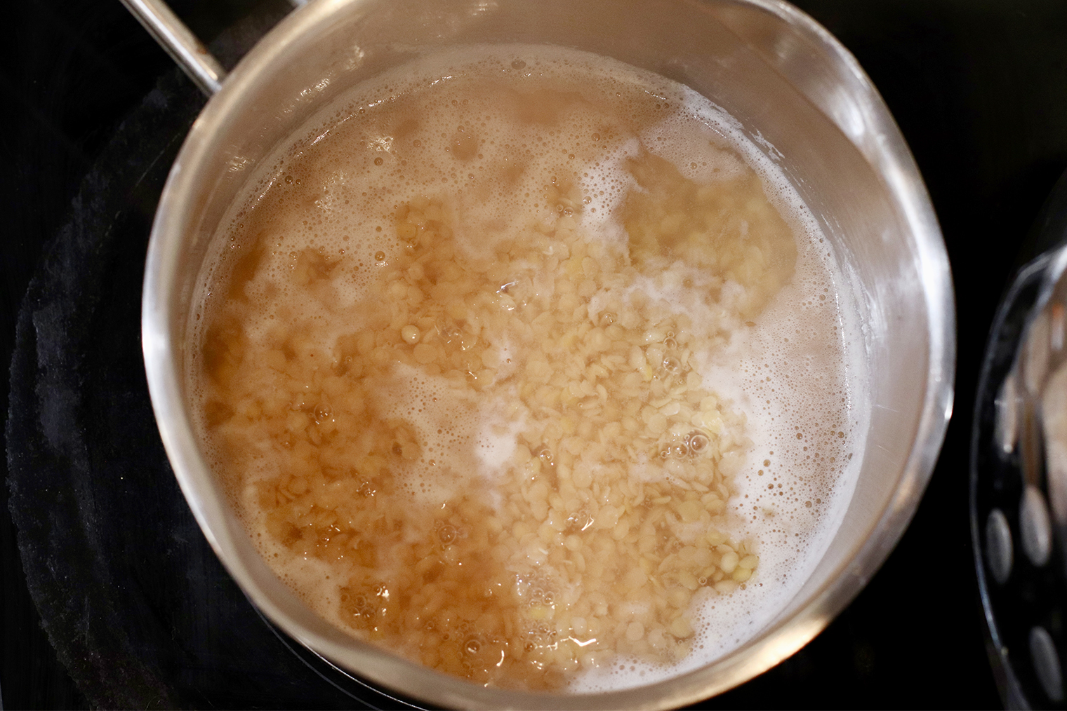 Шаг 2. Чечевицу поставьте на средний огонь и доведите до кипения. Зерна дадут пену — снимите ее ложкой. Уменьшите огонь до слабого и прикройте крышкой, оставив зазор для выхода пара. Готовьте 15 минут, периодически помешивая