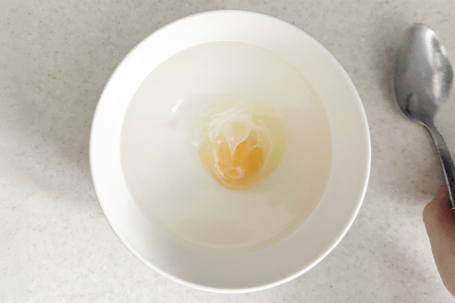 Шаг 2. Холодное яйцо разбейте в отдельную маленькую пиалу. Горячую воду в миске размешайте ложкой, чтобы сделать воронку. Аккуратно добавьте яйцо в воду