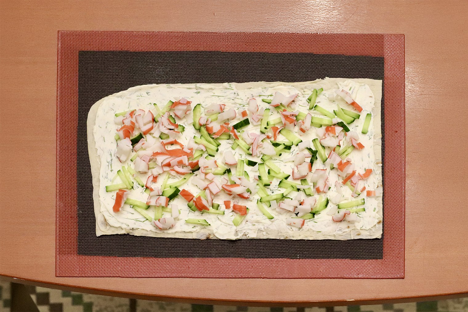 Шаг 3. Лаваш нарежьте листами размером 15 × 30 см. Половину сырной массы равномерно распределите по первому слою. Разложите поверх половину огурцов и палочек