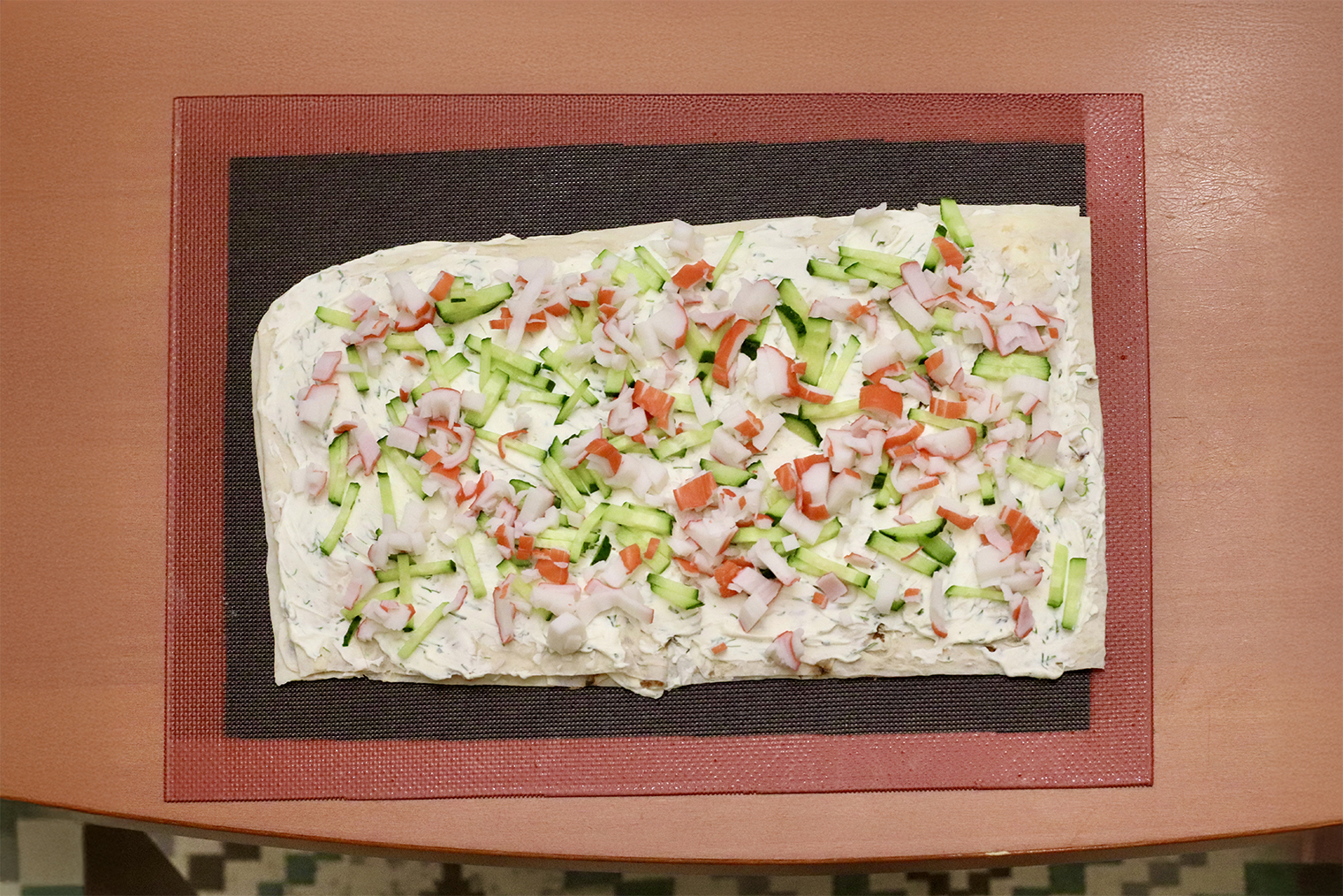 Шаг 4. Начинку накройте вторым листом лаваша. Смажьте его сырной массой, разложите вторую половину крабовых палочек и огурцов