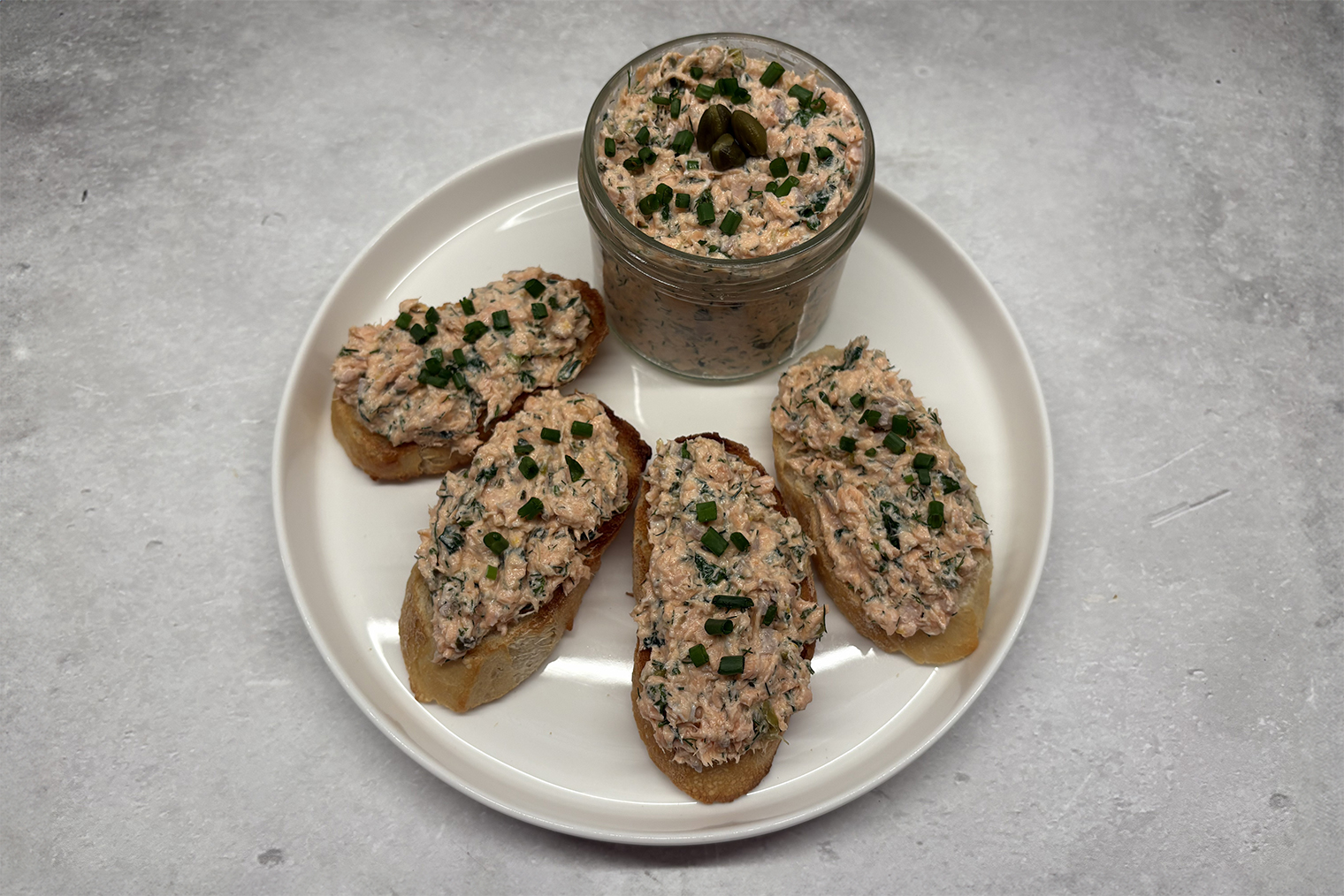 Шаг 4. Лосося, сливочный сыр, мягкое сливочное масло, каперсы, зелень, цедру и сок лимона соедините в миске. Посолите и перемешайте. Переложите риет в герметичный контейнер и уберите в холодильник на 1 час