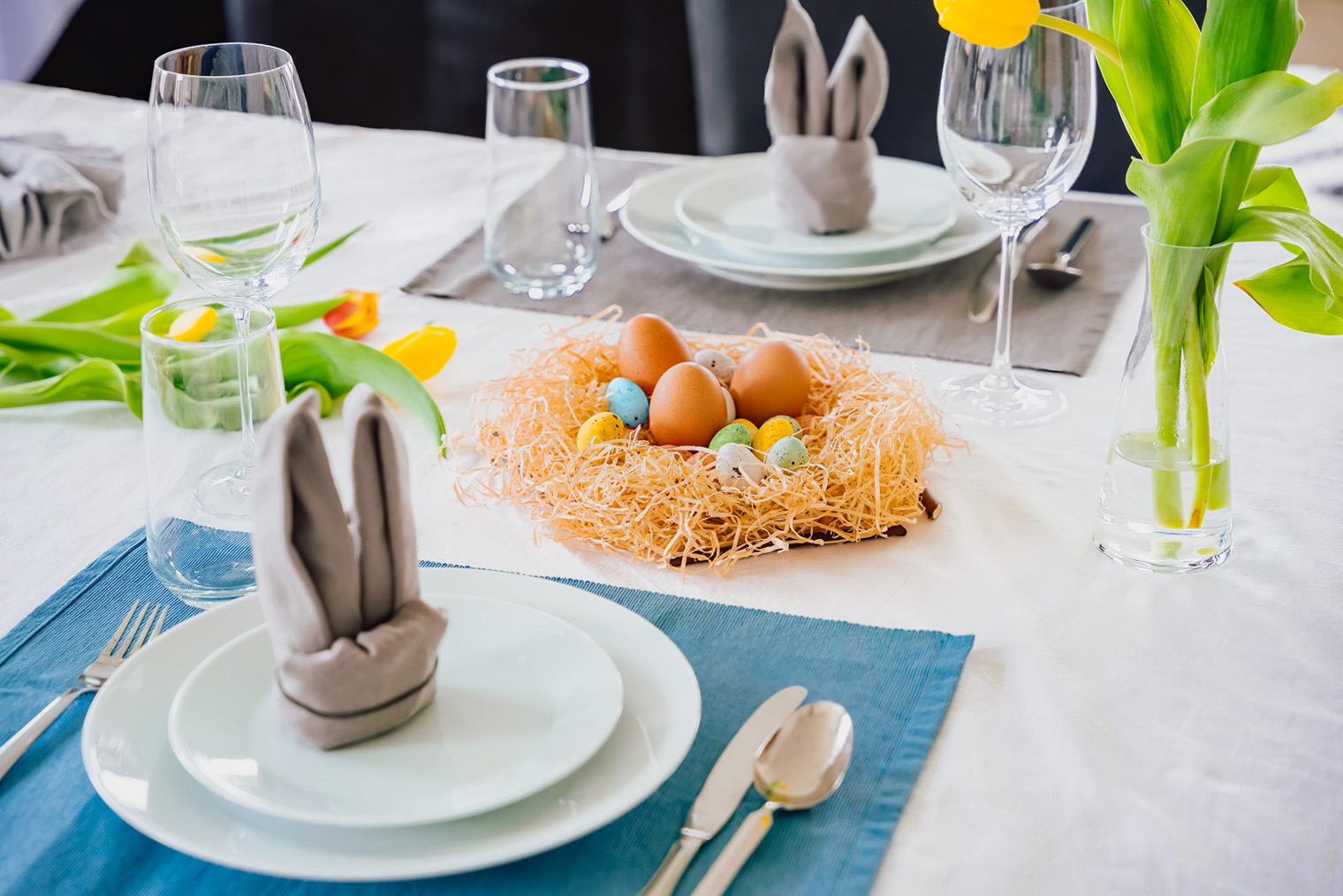 Пасхальная тематическая сервировка. Стол украшен гнездом с крашеными яйцами, а салфетки сложены в форме кроличьих ушек. Фотография: Jannissimo / Shutterstock / FOTODOM