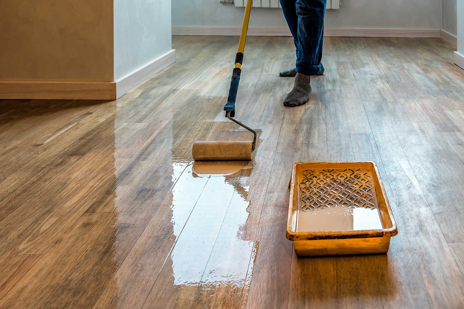 Лак наносят на деревянный пол валиком на длинной ручке. Это удобнее и быстрее, чем кистью. Фотография: Vova Shevchuk / Shutterstock / FOTODOM