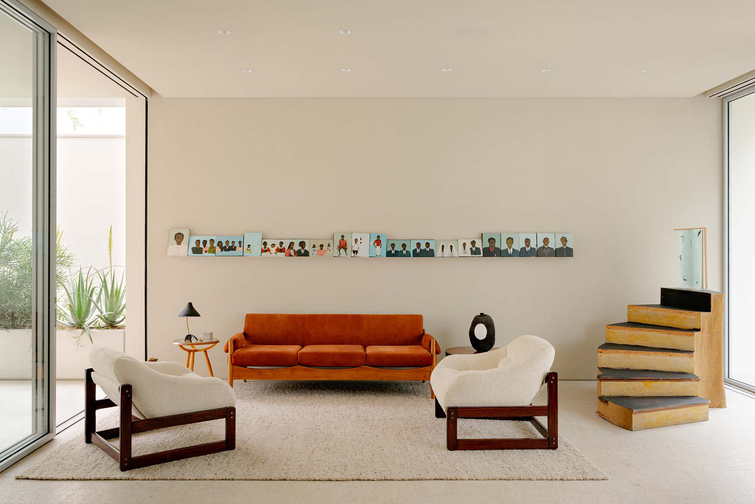 Светлые стены и пол создают спокойную основу, на которой яркий диван работает как композиционный центр. Он становится главной точкой, вокруг которой организовано пространство. Более темные основания кресел и яркие фотографии на стене балансируют композицию. © felipehess.com.br