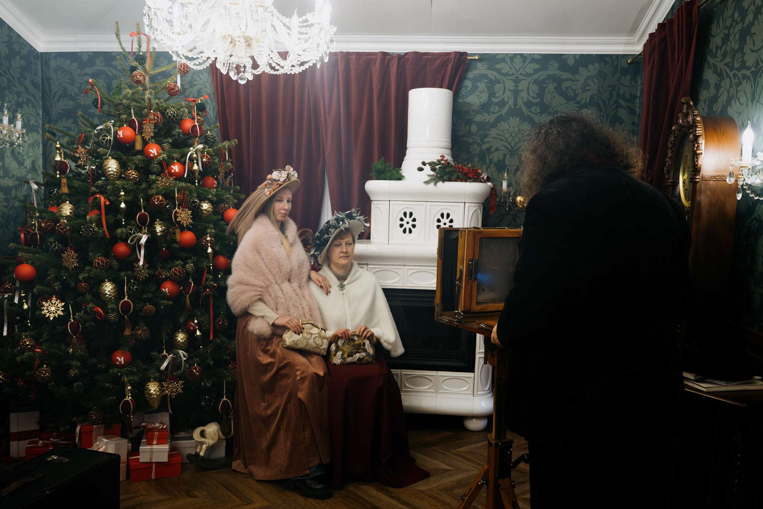 В фотозоне, которая находится в помещении, гостей фотографируют на фоне елки и старинной печи