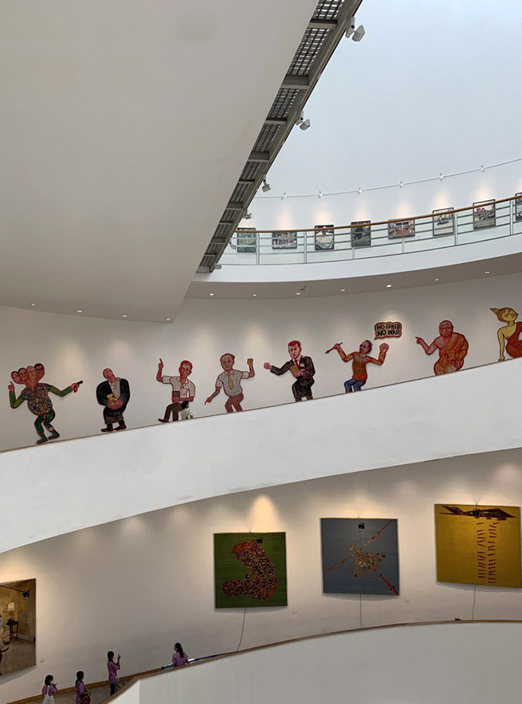 Экспозиции в BACC во время биеннале 2022 года. Внизу — ковры Яна Ката, выше — деревянные марионетки тайского художника Васана Ситтикета