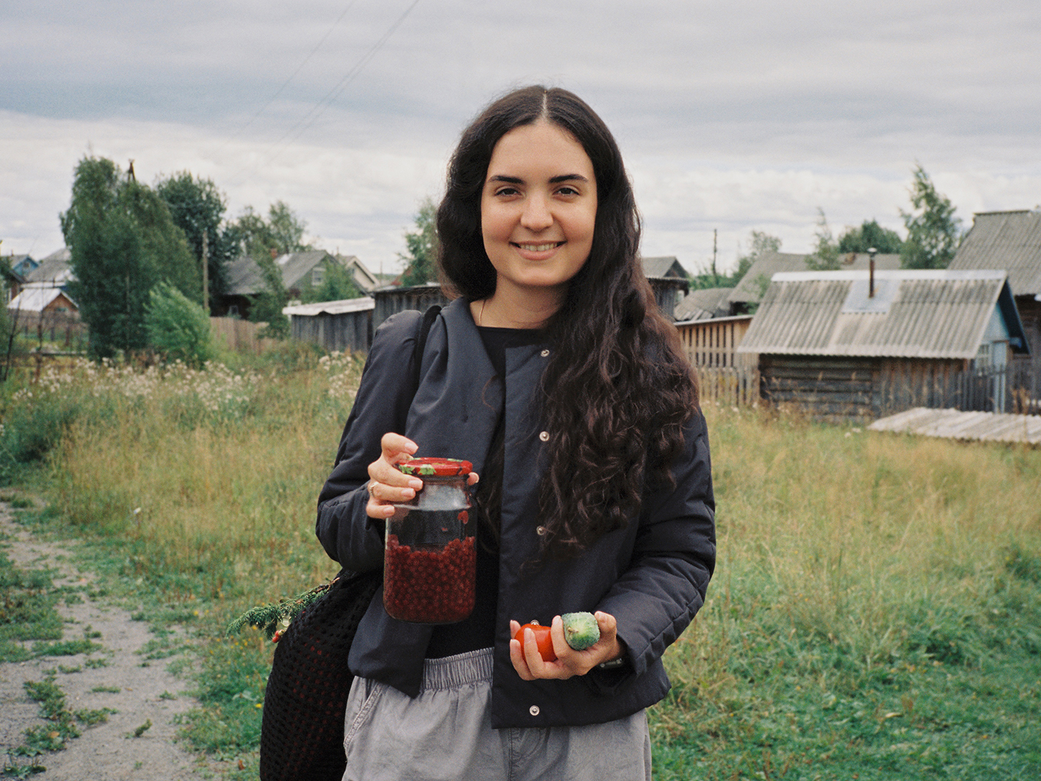 Лиза Аньшина, музыкальный руководитель «Толóка». В руках у нее домашние огурцы и помидоры, а еще — полбанки брусники, которые ей на дорожку заботливо дала Елена Васильевна Едошина