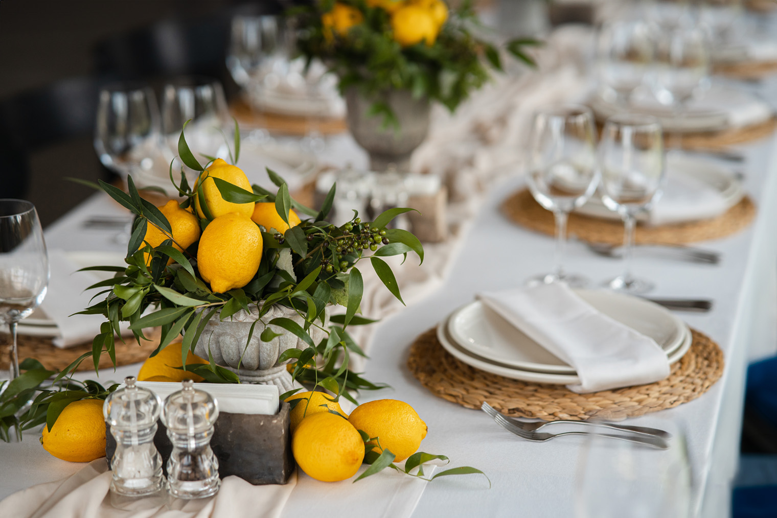 А этот — вазами с лимонами, которые хорошо сочетаются с плетеными плейсматами. Такие нейтральные плейсматы допустимы в классической сервировке. Фотография: Hrecheniuk Oleksii / Shutterstock / FOTODOM