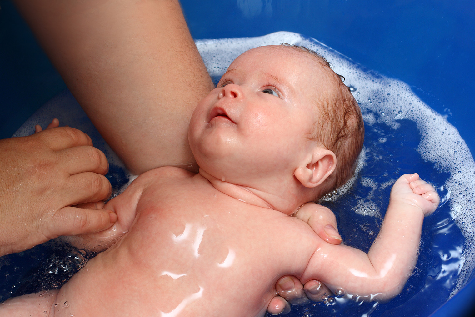 Во время купания в ванночке нужно завести руку за спину ребенка и постоянно поддерживать голову и шею. Чтобы крепче ухватить малыша, можно держать его за противоположное плечо. Вторая рука при этом будет свободна. Фотография: Mik122 / iStock