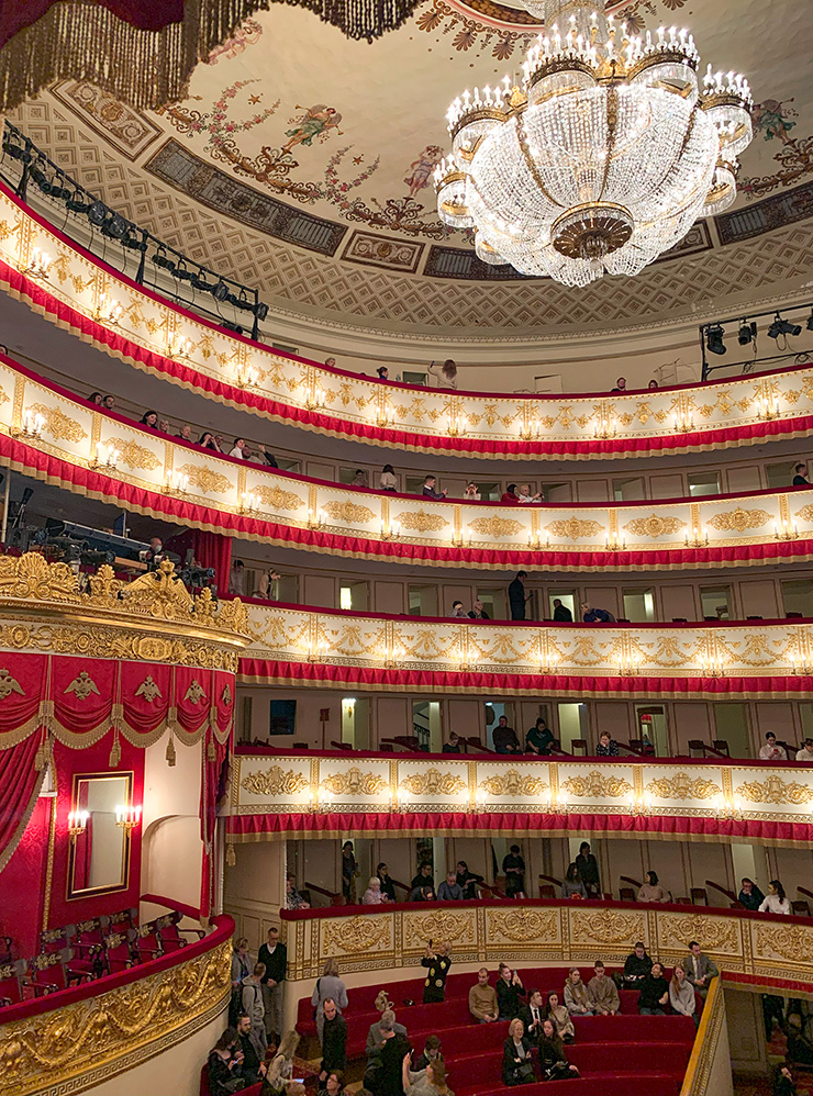 Зрительный зал Александринского театра выглядит торжественно и нарядно: ложи отделаны бархатом и украшены золоченой резьбой