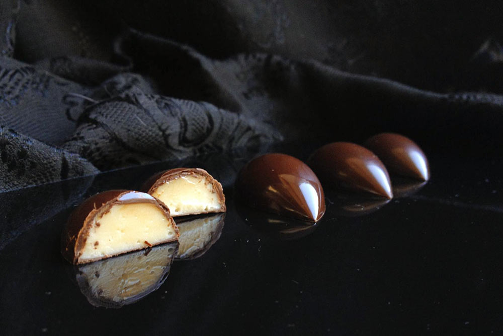 Корпусные конфеты из темного шоколада с начинкой из манго и маракуйи, ароматизированной бобами тонка. Корпус красиво блестит и не сразу тает в руках — значит, шоколад темперирован правильно