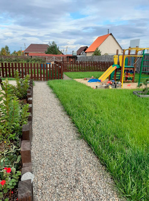 Дорожка перед домом и детская площадка, за забором — огород