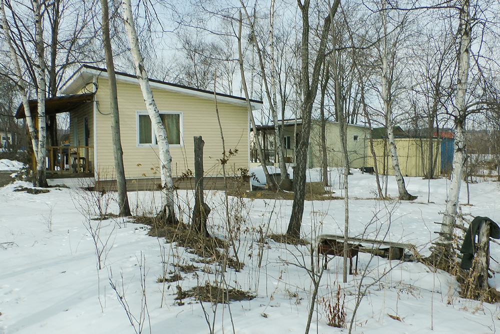 Слева дом, правее баня и контейнеры. На переднем плане летняя площадка для барбекю