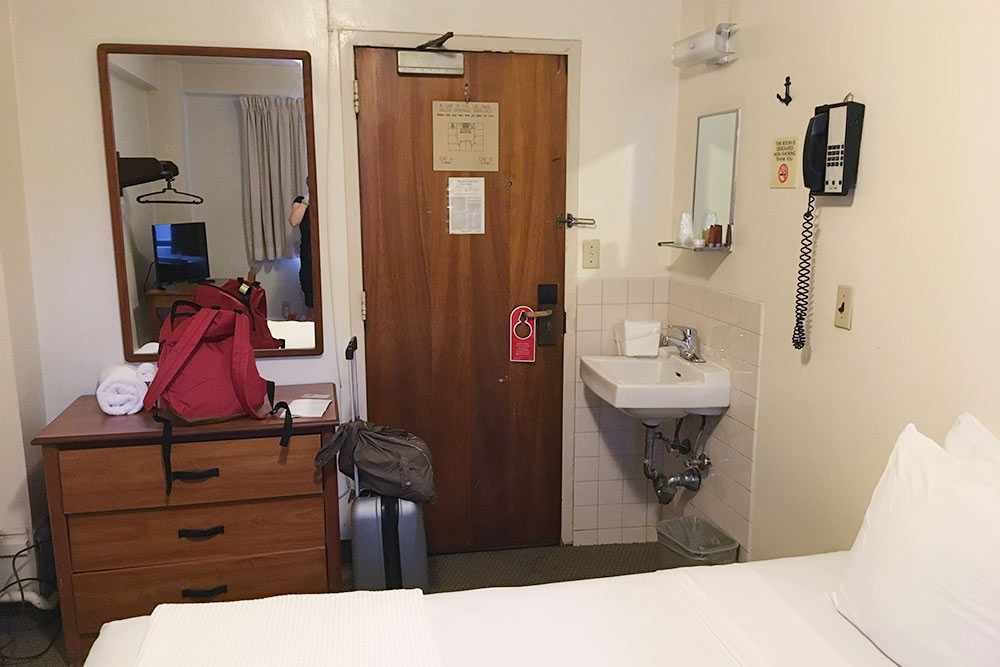 Комната в гостевом доме примерно за 99 $ (6930 ₽) в сутки. Здесь есть одноместная кровать, раковина, комод и шумный кондиционер. На этаже — два туалета и две душевых на десять комнат