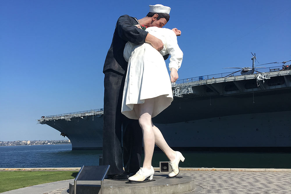 Это скульптура «Безоговорочная капитуляция», а на заднем плане — авианосец USS Midway
