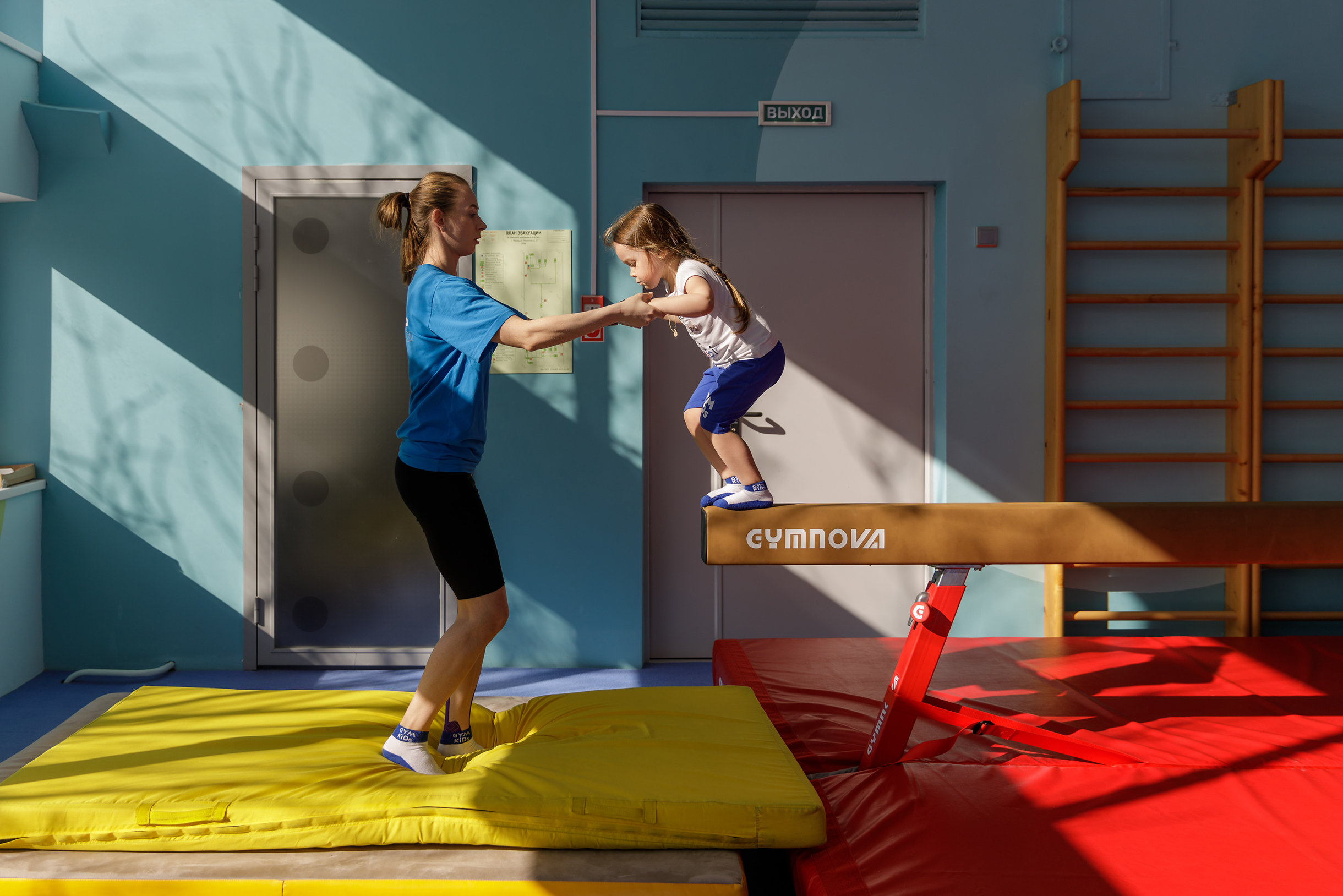 Ребенок выполняет гимнастическое упражнение под руководством тренера