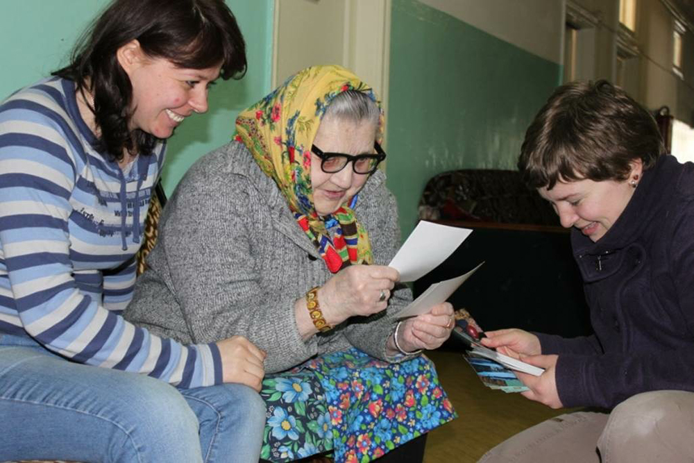 Волонтеры Нина и Марина в Няндомском доме престарелых смотрят вместе с Марией Петровной фото с предыдущей встречи. Это 2011 год