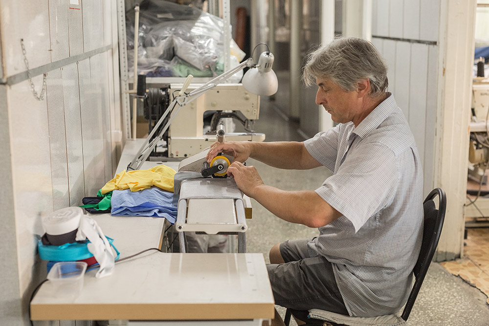 Разнорабочий — это самый универсальный сотрудник цеха. На фото он нарезает окантовку для обработки воротников на футболках