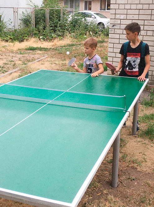 Дети учатся играть в настольный теннис во дворе дома