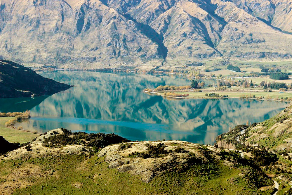 Гладкая поверхность воды озера Ванака отражает окружающие пейзажи