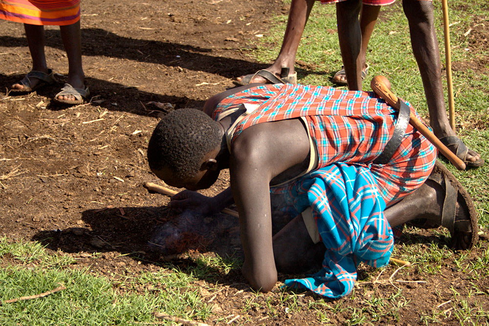 Масаи носят традиционную одежду — в Кении часто можно встретить людей в нарядах из красной ткани. Этот молодой человек показывает нам, как разводить огонь