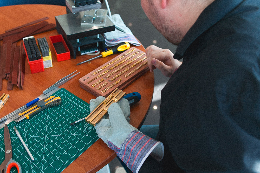 На мастер-классе по созданию кожаных браслетов показывают, как набирать в штамп на двойной оснастке символы для тиснения