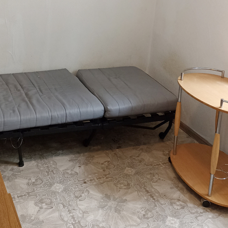 Левая сторона комнаты: раскладушка из «Икеи», столик на колесиках