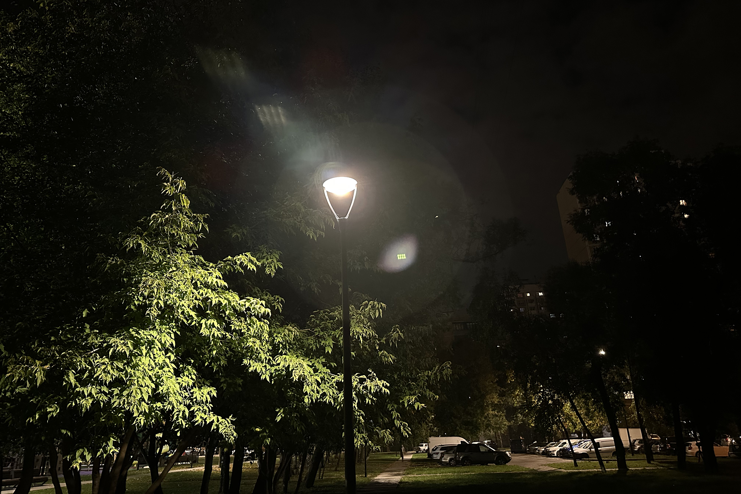 Сложная ночная сцена: яркий фонарь проработан достаточно четко, а на фоне в темноте хорошо видно дерево слева и дом справа. Парковка на заднем плане не пересвечена