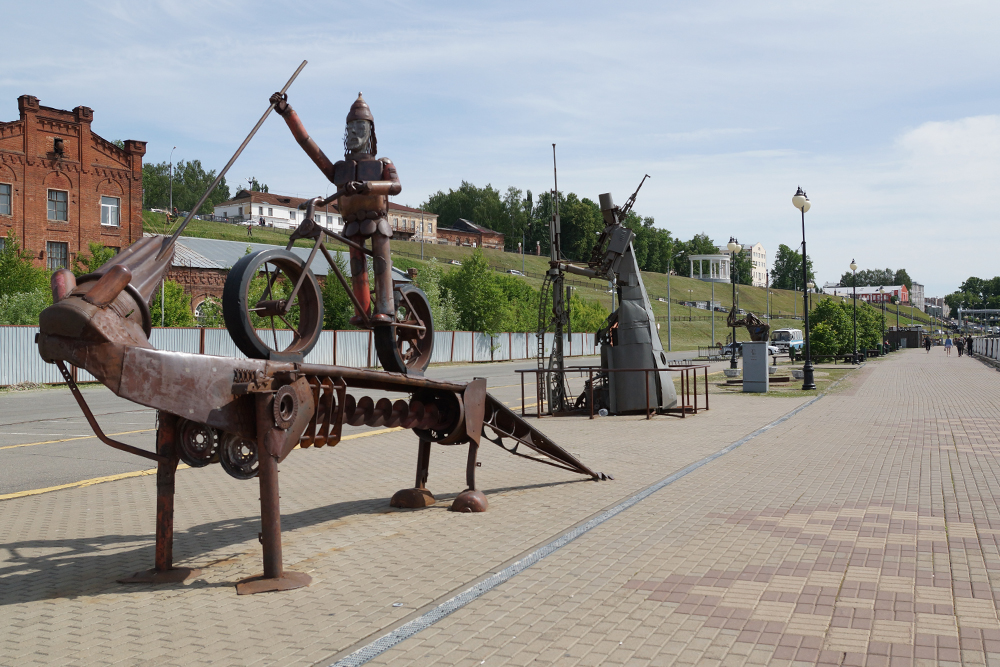 На набережной стоят скульптуры из металлолома, всего их десять. На переднем плане велосипедист, побеждающий змея